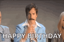 a man with a mustache is standing in front of a group of people and says `` happy birthday '' .