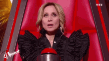 a woman in a black dress is sitting in a chair with a red button that says voice on it