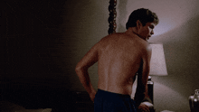 a man without a shirt is standing in front of a lamp