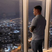 a man standing in front of a window looking out at a city