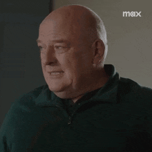 a bald man in a green shirt is looking at the camera .