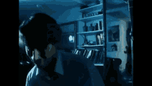 a man is standing in a dark room in front of a bookshelf and a window .