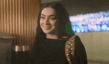 a woman wearing a black shirt and a brown purse is smiling in a room .