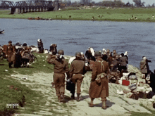 a group of soldiers are walking along the shore of a river with a sign that says kronos media
