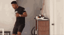a man is dancing in a room in front of a dresser with shoes on it .