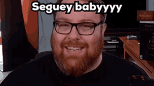 a man with glasses and a beard is smiling with the words segui babyyyy above him