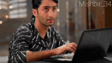 a man in a black and white striped shirt is typing on a laptop with the hashtag mishbir_34 above him