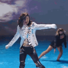 a man in a white jacket is dancing on a blue stage