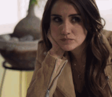 a woman wearing a tan jacket has her hand on her face