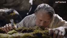 a man is laying on the ground with his mouth open and smelling moss .
