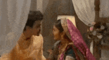 a man and a woman are sitting on a bed and looking at each other .
