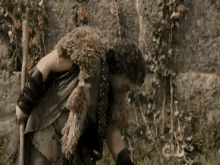 a man in a fur coat is standing in the grass holding a stick .
