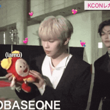 a man in a suit holds a stuffed animal in front of a sign that says kcon