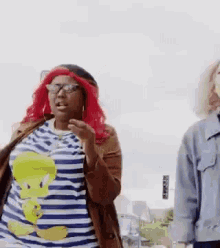 a woman with red hair and glasses is standing next to another woman wearing a tweety bird shirt .