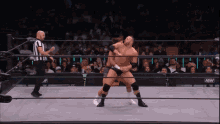 two men are wrestling in a ring with a referee in the background .