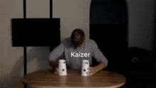 a man is sitting at a table stacking cups on top of each other with the word kaizer on the bottom .