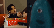 a man is sitting at a table eating food with chopsticks next to a blue monster with a big eye .