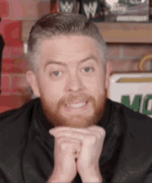 a man with a beard and mustache is smiling with his hands folded .