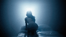 a woman is kneeling down on a bed in a dark room