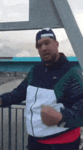 a man wearing a nike jacket and a blue hat stands on a bridge