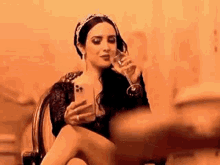 a woman is sitting in a chair holding a glass of wine and looking at her phone .