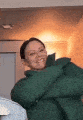 a woman wearing a green jacket is smiling and hugging herself