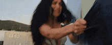 a woman with long black hair is holding a man 's shirt in her hands .