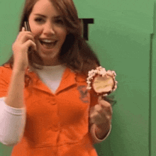 a woman in an orange shirt is talking on a cell phone and holding a lollipop