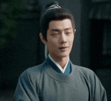 a man with a bun on his head is wearing a blue robe and a white shirt .