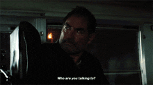 a man in a dark room is talking to someone and they are asking who are you talking to