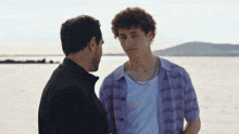 a man in a plaid shirt is talking to another man in a white shirt
