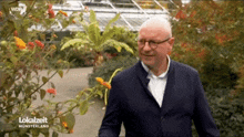 a man stands in front of a greenhouse with the words lokalzeit munsterland written on the bottom
