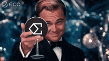 a man in a tuxedo is holding a glass with a circle with the letter s on it in front of his face