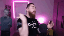a man with a beard is dancing in front of a microphone in a room with pink lights .