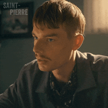 a man with a mustache is sitting in front of a wall with saint-pierre written on it