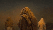 a man in a hooded robe is walking through a desert .