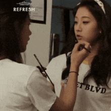 a woman applying makeup to another woman wearing a shirt that says blvd