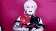 a woman in a harley quinn costume is standing with her arms crossed on a pink background .