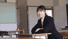 a girl in a suit sits at a desk in a classroom smiling