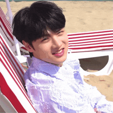 a young man sits in a red and white chair on the beach