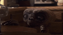 a small brown alien is sitting at a table in a kitchen .