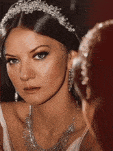 a woman wearing a headband and a necklace looks at her reflection in a mirror