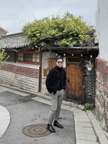 a man wearing glasses stands in front of a building with a greek key pattern