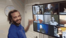 a man in a blue shirt is standing in front of a large tv screen with a group of people on it .