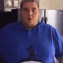 a man in a blue shirt is standing in front of a refrigerator and a microwave .