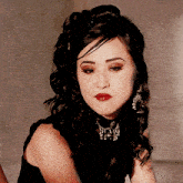 a woman with dark hair and red lips is wearing a black top and earrings