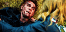 a man with blood on his face is laying in the grass with a woman holding him .