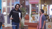 two men are standing next to each other in front of a food stand sponsored by sony television