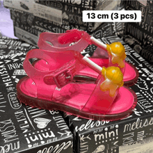 a pair of pink sandals with a yellow lollipop on a black box that says 13 cm ( 3 pcs )