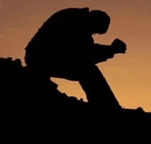 a silhouette of a man kneeling down with his hands folded in prayer .